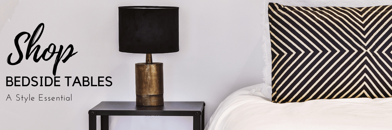 Bedside table with a lamp and books beside a made bed