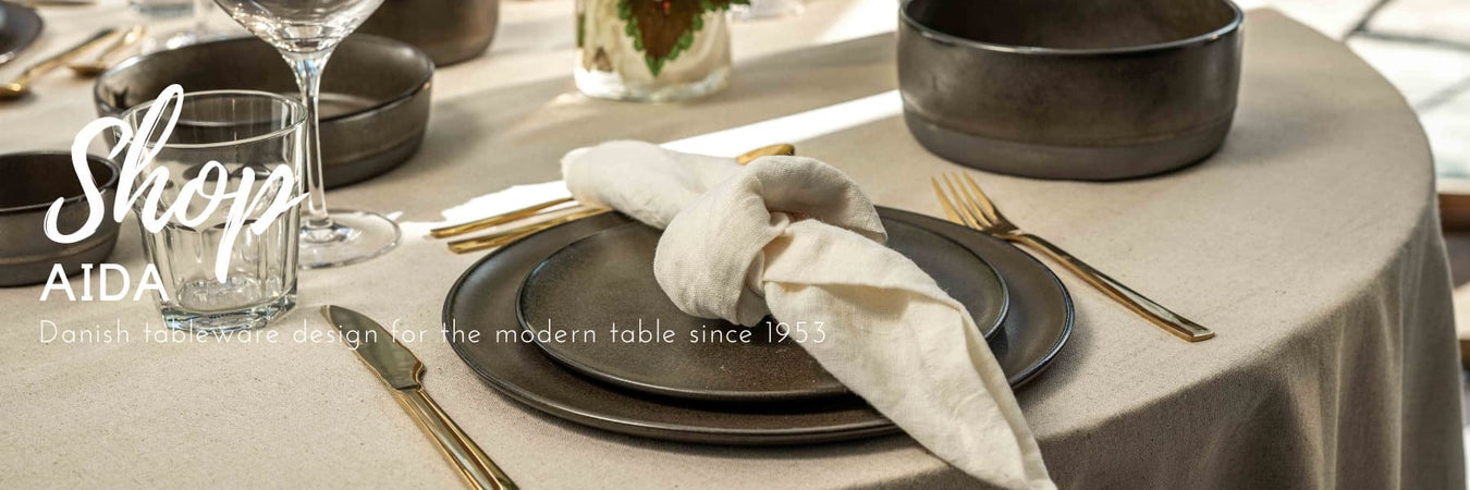 Elegant dining table featuring Aida Danish tableware in charcoal tones, styled with gold cutlery, crystal glassware and soft linen textures. A timeless Scandinavian tablescape designed for modern entertaining. lghting.co.za
