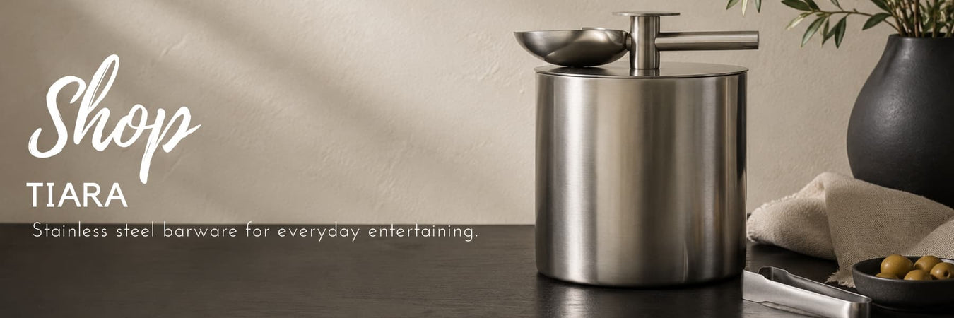 Tiara stainless steel barware featuring a brushed stainless steel ice bucket and serving accessories, styled in a modern entertaining setting. Elegant essentials for everyday hosting.