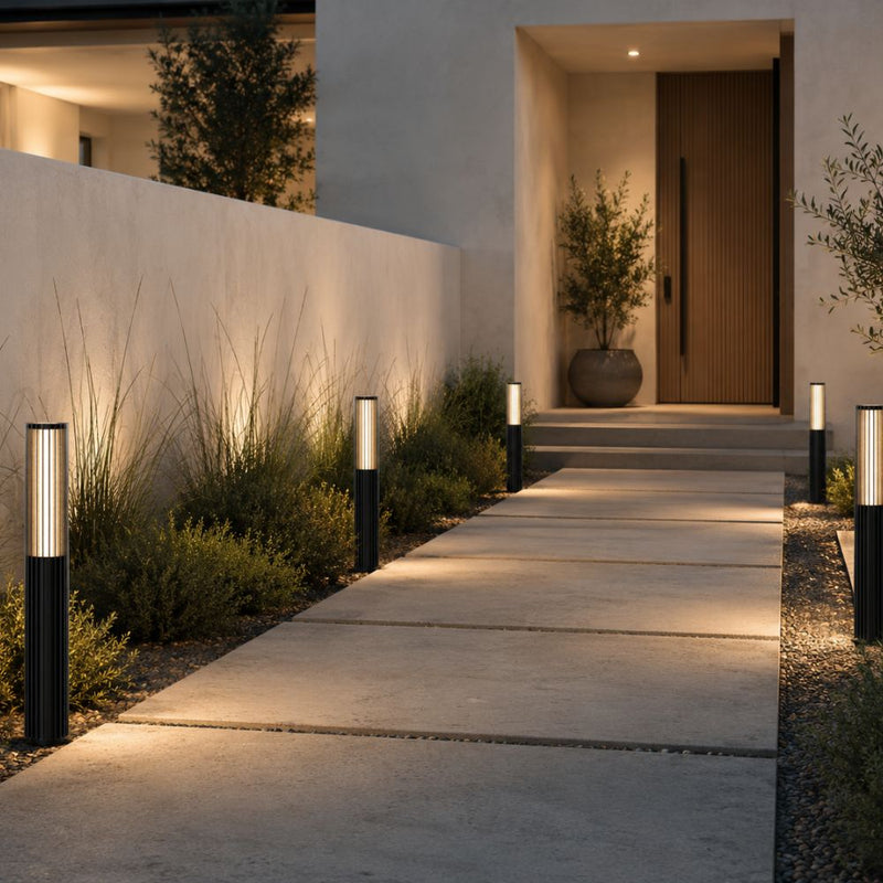 Modern outdoor pathway lighting with multiple black cylindrical bollard lights illuminating a concrete walkway leading to a house entrance at dusk - Lighting.co.za