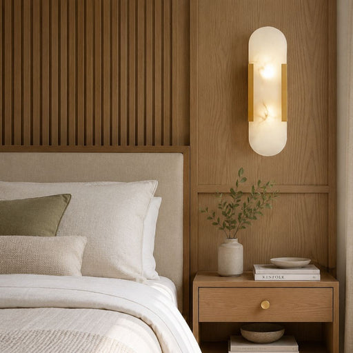 Gold and marble wall light illuminated above a wooden bedside table in a warm contemporary bedroom with soft neutral bedding and natural daylight – Lighting.co.za