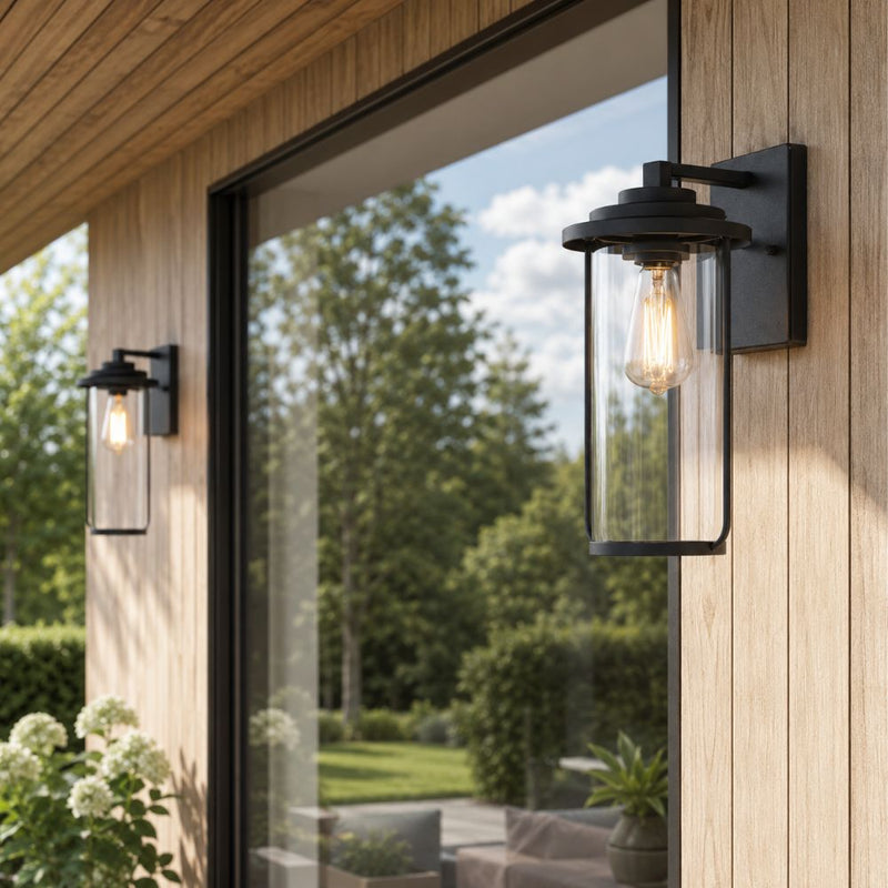 Black outdoor wall sconces mounted on a wood-clad building exterior, with one shown in close-up on the right and another visible in the background on the left, overlooking a green garden - Lighting.co.za