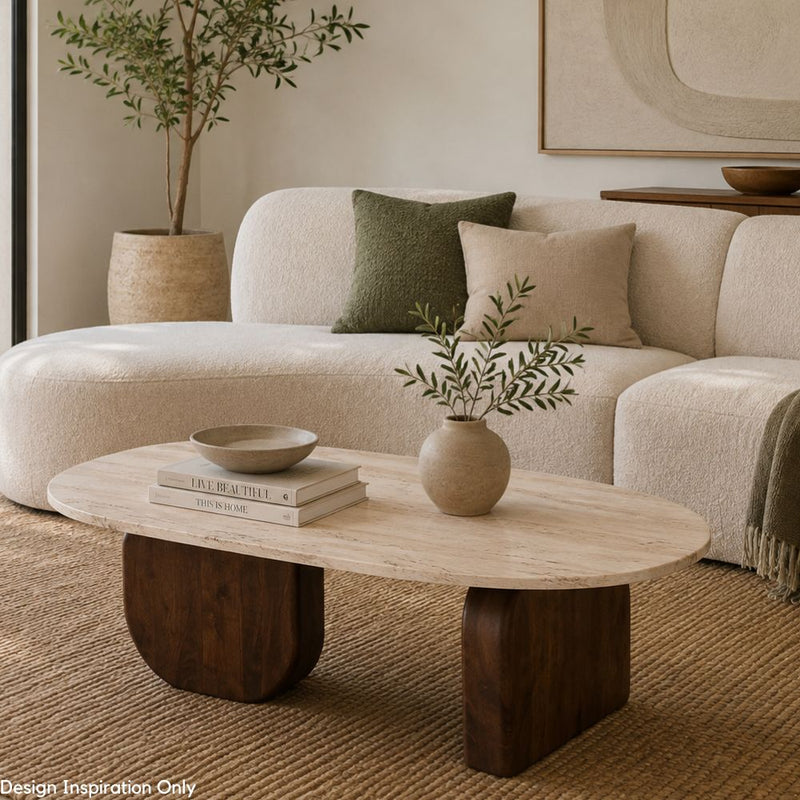 An oval coffee table with a light beige stone top and dark brown block legs in a styled living room. The table is styled with a small ceramic vase containing greenery, a bowl, and stacked books, with a cream boucle sofa and neutral pillows in the background - Lighting.co.za