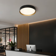 A modern flush-mount ceiling light with a black outer ring, a gold inner accent, and a white diffuser, installed on a white ceiling in a contemporary office space.