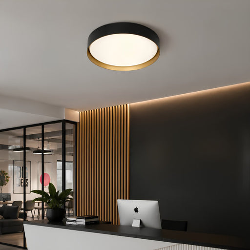 A modern flush-mount ceiling light with a black outer ring, a gold inner accent, and a white diffuser, installed on a white ceiling in a contemporary office space.