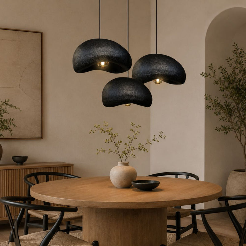 Three black textured pendant lights hanging over a round wooden dining table in a warm, modern interior setting - Lighting.co.za