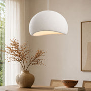 Modern dining room with a sculptural natural rattan pendant light glowing above a black round pedestal table, surrounded by oak and cane dining chairs, earthy ceramic décor, abstract wall art, and soft natural daylight – Lighting.co.za