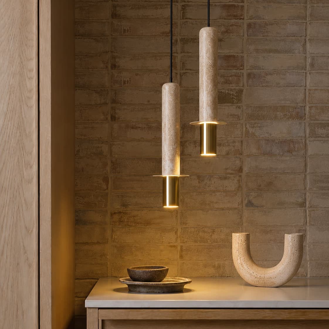 Two modern pendant lights with cylindrical beige stone or wood shades and gold-toned metal accents, hanging over a wooden console table in a warm interior setting. Pendant Light Buying Guide - Lighting.co.za