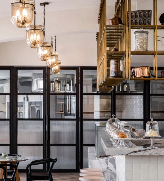 Warm glass pendant lights in a modern café with marble counters and black framed cabinetry – Lighting.co.za