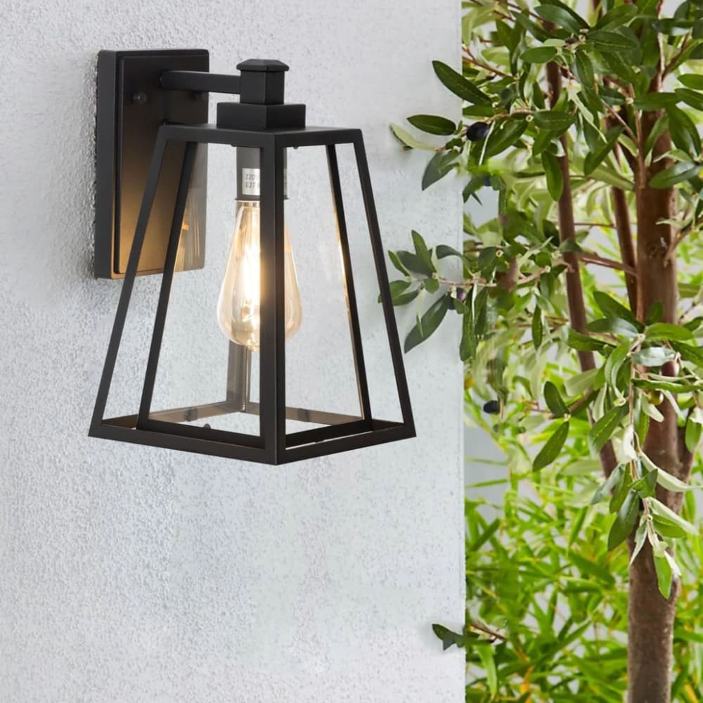 Black outdoor wall light fixture on a light gray wall with green foliage in the background. Outdoor Lighting Buying Guide - Lighting.co.za