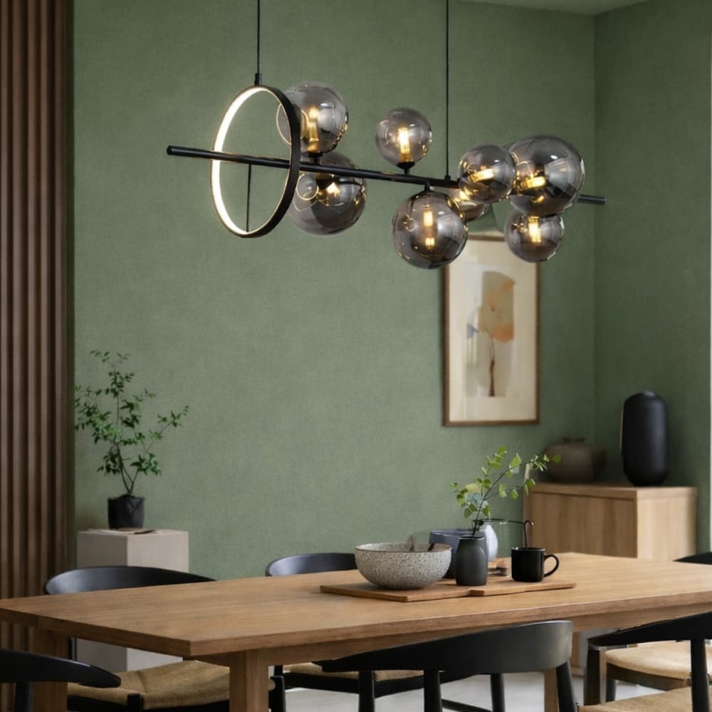 Modern black and smoke glass pendant light hanging above a dining table with a green wall and decor in the background. Pendant Light buying guide - Lighting.co.za