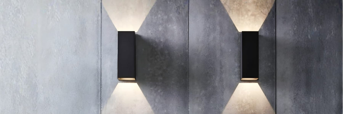Two modern black rectangular wall sconces mounted on a textured gray concrete wall, casting warm light downward in a symmetrical arrangement. Outdoor Lighting Buying Guide - Lighting.co.za