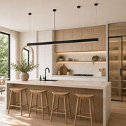 A modern kitchen island with a light wood fluted front, a white marble countertop, and four wooden bar stools. The background features light wood cabinets, a black linear LED pendant light, and a large window on the left - Lighting.co.za