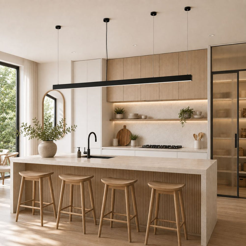 A modern kitchen island with a light wood fluted front, a white marble countertop, and four wooden bar stools. The background features light wood cabinets, a black linear LED pendant light, and a large window on the left - Lighting.co.za